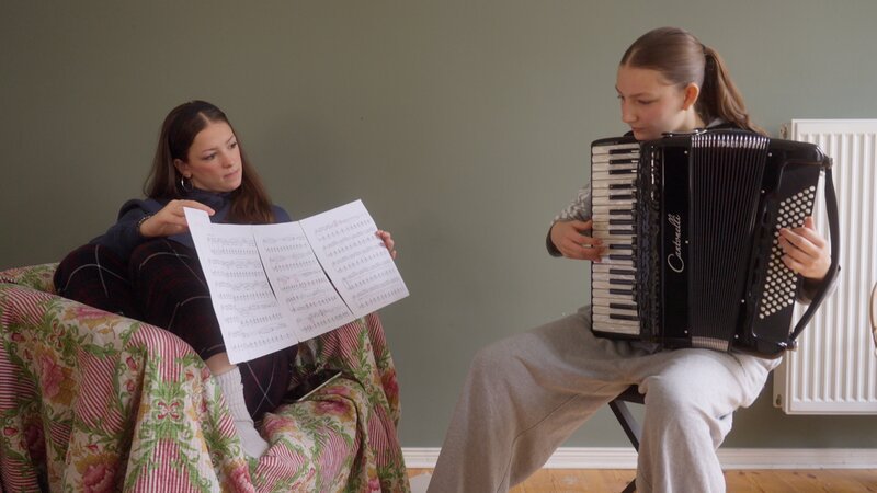Jojo hört Alma das erste Mal Akkordeon spielen. – Bild: NDR/​Telekult