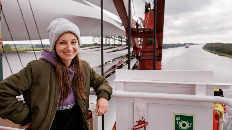 Checkerin Marina auf einem Frachtschiff im Nord-Ostsee-Kanal, das Rotorblätter für Windräder geladen hat. – Bild: BR/​megaherz gmbh/​Marina Hufnagel