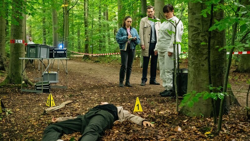 Während des Probenwochenendes einer Schützenkapelle wird die Dirigentin Nadja Schilling (Kaja Schmidt-Tychsen, l.) erschlagen im Wald aufgefunden. Dr. Westphal (Yulia Yáñez Schmidt, r.) erklärt den Kommissaren Jonas Fischer (Lukas Piloty, 2.v.r.) und Amira Mahdi (Aylin Ravanyar, 2.v.l.), dass der Tubist die Leiche gefunden hat. – Bild: ZDF und Martin Rottenkolber