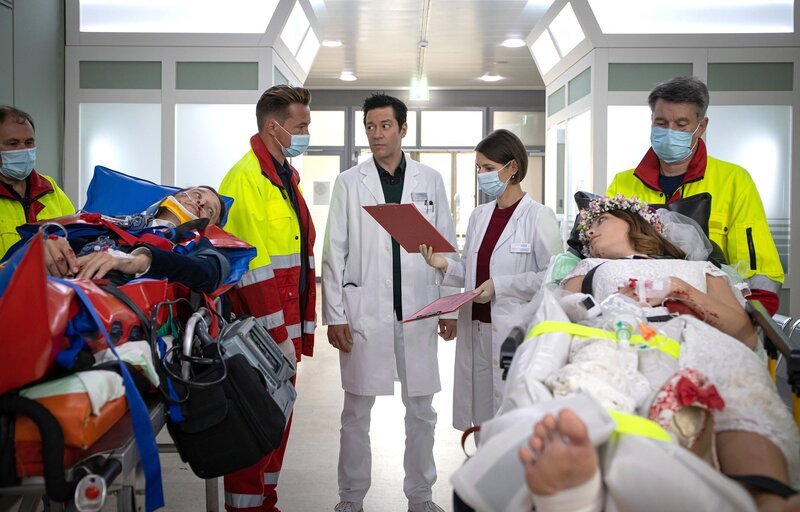 Nikki Schönau (Lena Meckel, re. liegend) und Hauke Friedrich (Oliver Konietzny, li. liegend) sind mit dem E-Roller auf dem Weg zum Standesamt verunglückt. Notarzt Dr. Lorenz (Markus Neumann, hi. li.) klärt Dr. Maria Weber (Annett Renneberg, hi. re.) und Dr. Philipp Brentano (Thomas Koch, hi. mi.) über die festgestellten Verletzungen auf. – Bild: MDR/​Saxonia Media/​Rudolf Wernicke