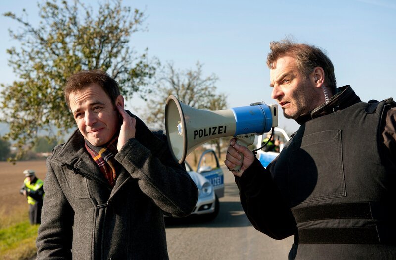 ARD HEITER BIS TÖDLICH – ALLES KLARA, FOLGE 11, „Mordwaffe Trabi“, am Donnerstag (12.07.12) um 18:50 Uhr im ERSTEN. Walter Stichling (Heinrich Schafmeister, r.) traktiert Paul Kleinert (Felix Eitner, l.) mit dem Megaphon. – Bild: ARD/​Marion von der Mehden