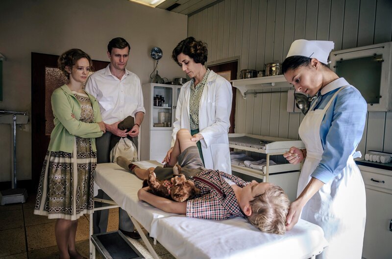 Kinderlähmung? Im Beisein seiner Eltern (v.l.n.r. Anne Kanis, Ulrich Friedrich Brandhoff) untersuchen Kinderärztin Dr. Ingeborg Rapaport (Nina Kunzendorf, 2.v.r.) und Schwester Arianna (Patricia Meeden, r.) den kleinen Werner Simoneit (Hugo Gross, 2.v.r.). – Bild: ARD/​Stanislav Honzik /​ ARD-Programmdirektion