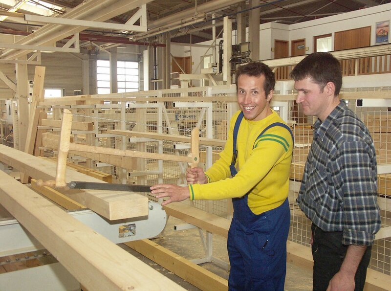 Ein Zimmermann erklärt Willi Weitzel seine Arbeit. Hier entstehen Holzbalken für die Wände eines Fertighauses. – Bild: BR/​Megaherz GmbH