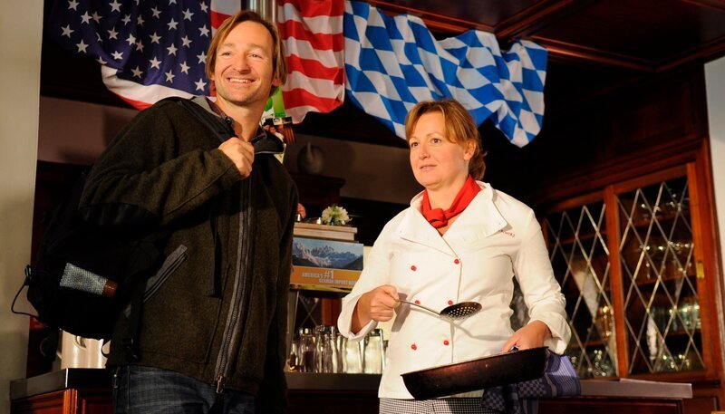 Gregor staunt über den amerikanischen Brunnerwirt. Von links: Gregor (Holger M. Wilhelm) und Veronika Brunner (Senta Auth). – Bild: BR/​Jo Bischoff