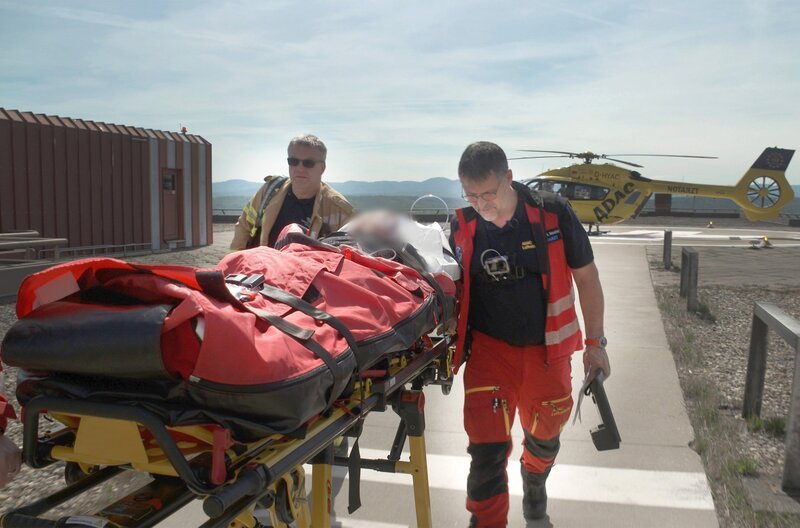 Rettungshubschrauber Christoph 22 auf dem Dach der Uniklinik Ulm. Ein Mitarbeiter des Brandschutzes begleitet Notarzt Dr. Björn Hossfeld beim Transport eines Patienten. – Bild: SWR