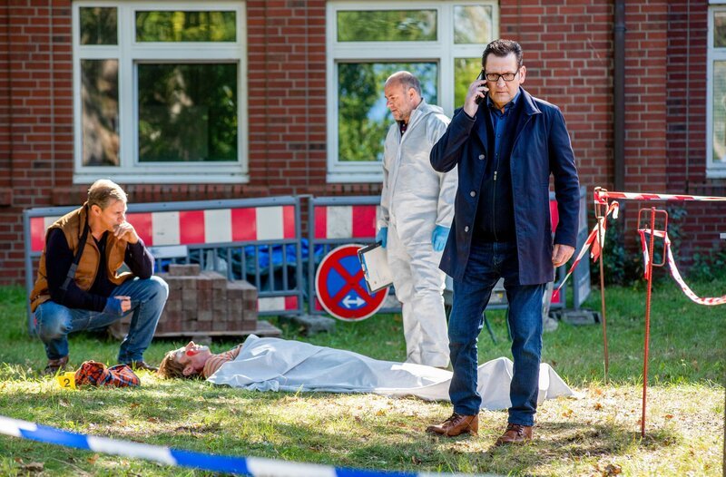 Der Krankenhausclown Fidan Petrov (Philipp Boos, liegend) liegt erschlagen im Hinterhof der Klinik. Die Kommissare Finn Kiesewetter (Sven Martinek, l.) und Lars Engel (Ingo Naujoks, r. mit Christoph Tomanek, 2.v.r.) ) finden heraus, dass der Tote ein Betrüger war. – Bild: ORF/​ONE GATE/​ARD/​Thorsten Jander