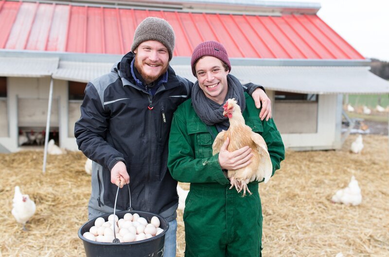 Checker Tobi (rechts) und Landwirt Georg Zankl mit einer Henne und Eiern. – Bild: BR/​megaherz gmbh/​Hans-Florian Hopfner