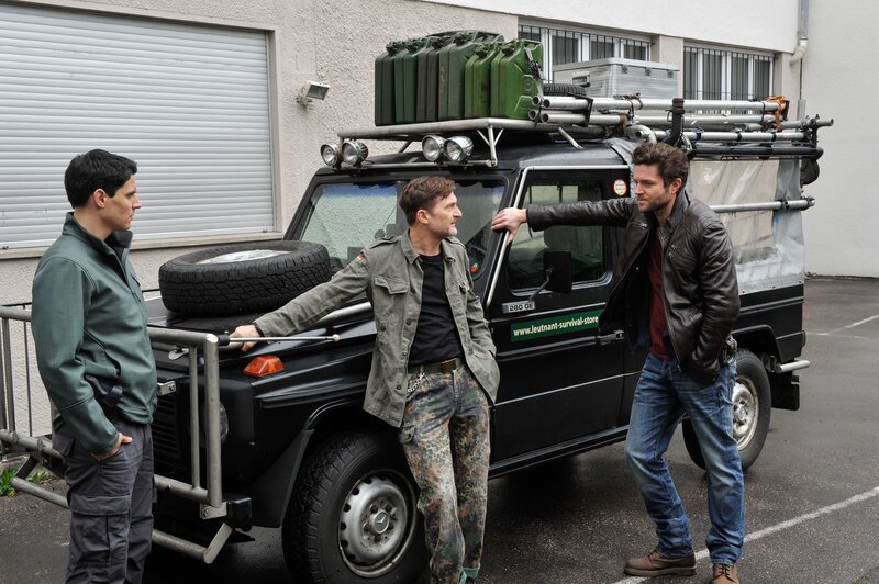 Eingekeilt zwischen Jo Stoll (Peter Ketnath, r.) und Rico Sander (Benjamin Strecker, l.) steht Philipp Leutnant (Jörn Hentschel, M.) Rede und Antwort. Dabei hat er seinen Survival-SUV fest im Griff. – Bild: ZDF und MARKUS-FENCHEL