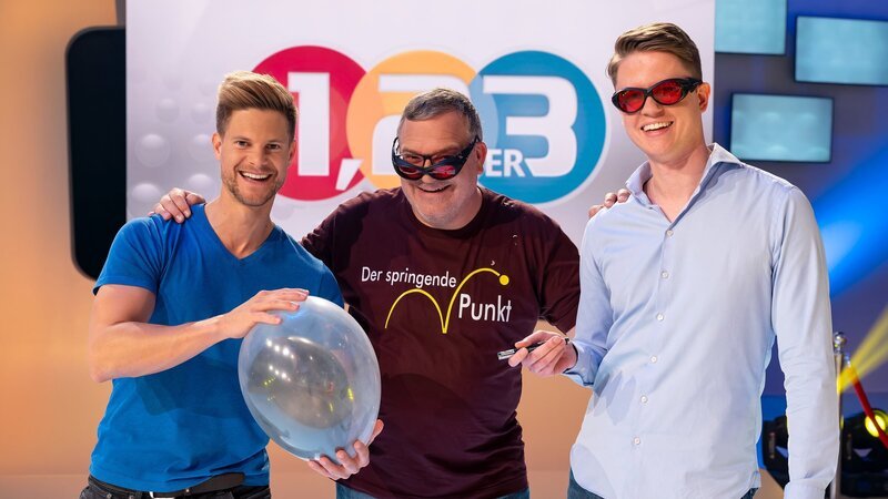 Die Physiker Dr. Philip Häusser (l.) und Moritz Heindl (r.) zeigen Elton in einem spektakulären Luftballon-Experiment, wie stark Laserstrahlen sein können. – Bild: ZDF und Ralf Wilschewski