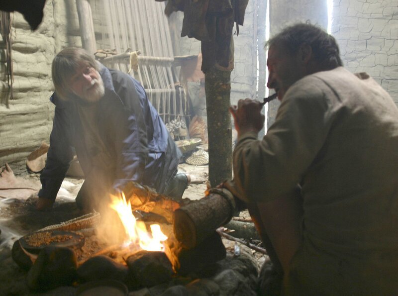 Der Steinzeit-Experte Harm Paulsen besucht die Sippe in regelmäßigen Abständen im Steinzeit Dorf. Hier mit Ingo Schuster an der Feuerstelle. – Bild: SWR/​Nowak