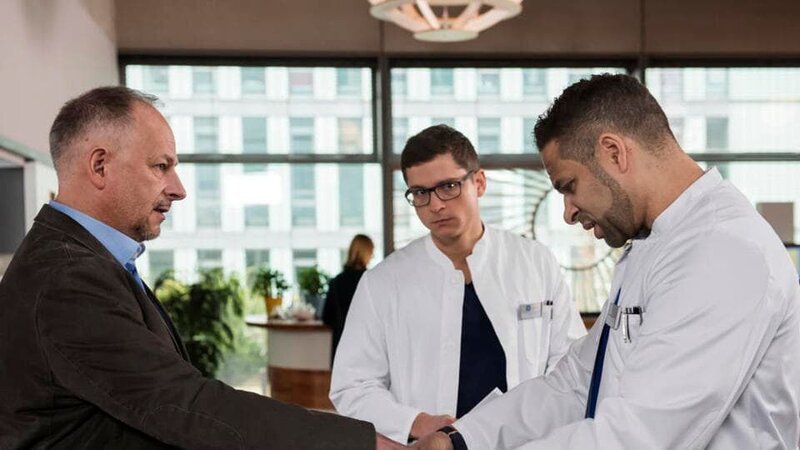Der Zahnarzt Dr. Daniel Möhring (Frank Röth, l.) hat sich die Hand gebrochen und sucht den fachlichen Rat von Dr. Moreau (Mike Adler, r. mit Stefan Ruppe, M.). – Bild: ARD/​Jens Ulrich Koch