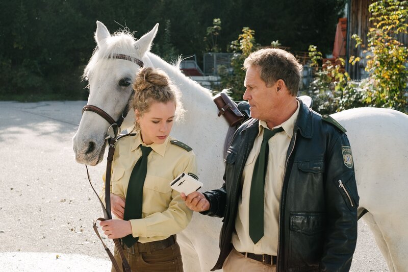 Das herrenlose Pferd mit dem Handy in der Satteltasche gibt Hubert (Christian Tramitz, r.) und Lena (Klara Deutschmann, l.) Rätsel auf. – Bild: TMG /​ Emanuel Klempa