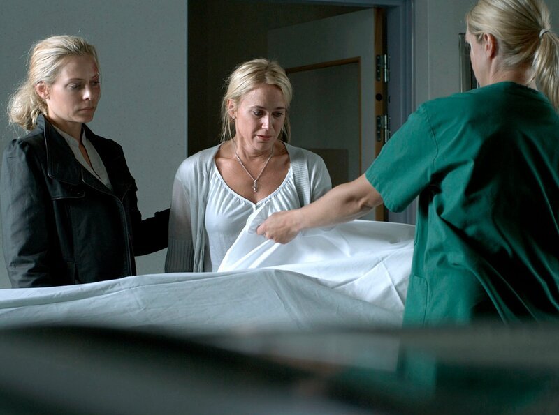 Maria (Eva Röse, links) steht Rosmarie (Anja Lundqvist, Mitte) zur Seite, die bei der Gerichtsmedizinerin Erika (Tanja Lorentzon, rechts) die Leiche ihres Mannes identifizieren muss. – Bild: ARD Degeto/​Eyeworks Film Gemini/​Calle Persson