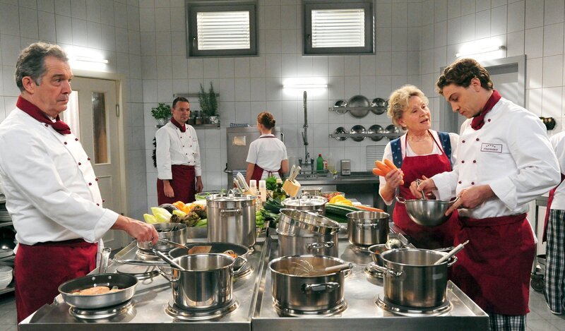 Als Christian (Leander Lichti, r.) für Elena einspringt, glaubt Hildegard (Antje Hagen, 2.v.r.), dass er ein guter Freund für Elena ist. André (Joachim Lätsch, l.) indes zeigt sich skeptisch (mit Komparsen, h.). – Bild: ARD/​Ann Paur