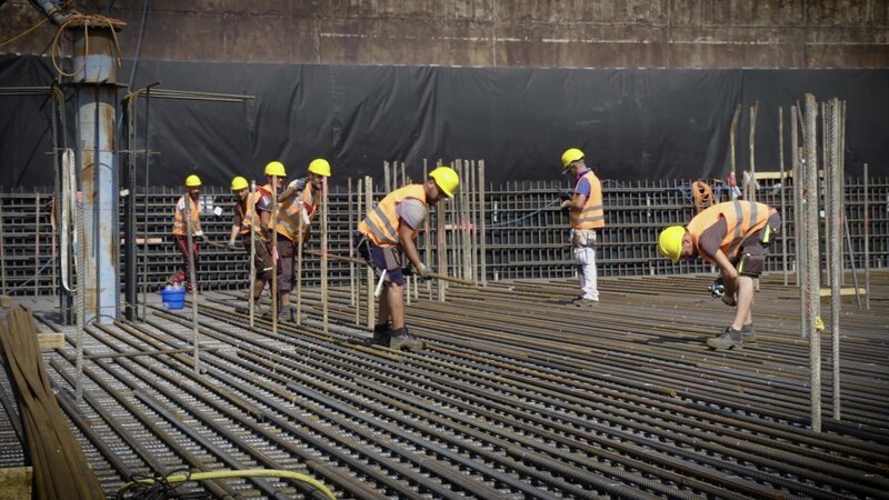 Auf der Baustelle im Inneren des Hochhauses verlegen Bauarbeiter millimetergenau tonnenschwere Stahlarmierungen. – Bild: WELT