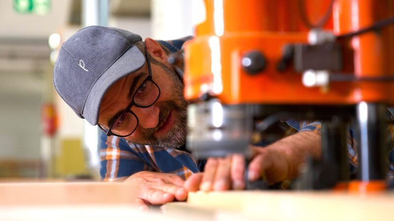 Ein Arbeiter führt eine Holzplatte durch eine Industriemaschine. – Bild: @Red Bull Media House/​ServusTV