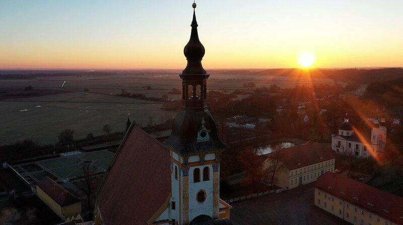 Das erste Mal seit dem Mittelalter wird in Deutschland ein neues Kloster gebaut. In der Diaspora; im Wald, wo früher ein Stasi-Erholungsheim war. Die Mönche zogen zuerst aus Österreich in die alte Klosteranlage Neuzelle – eine Touristenattraktion. Unverträglich mit monastischer Einkehr. Deshalb der Neubau. Der Film zeigt sie zwischen Gebet, Arbeit und Youtube-Clips bei strenger Kirchenlehre. – Sonnenaufgang über der barocken Klosteranlage in Neuzelle. – Bild: rbb/​Michael Lietz