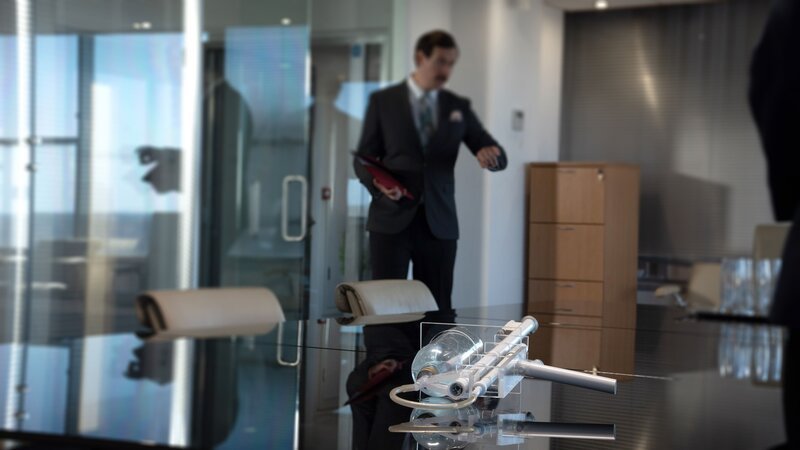 Eine Person im Anzug steht in einem modernen Büro, während ein technisches Gerät in einem transparenten Gehäuse auf dem Tisch liegt. – Bild: The HISTORY Channel