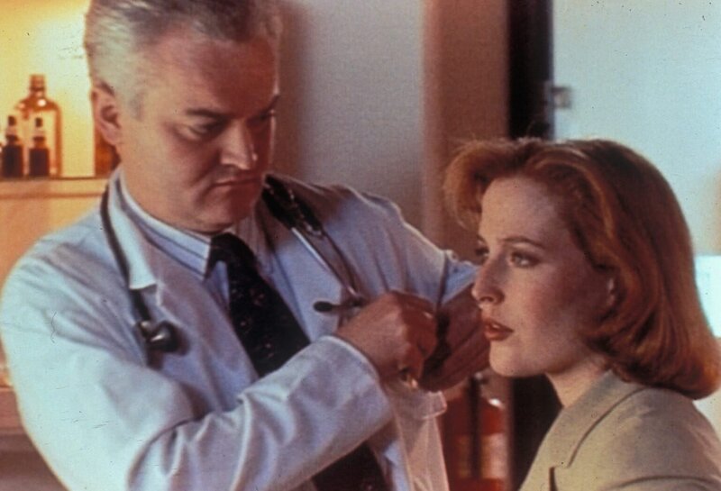 Nachdem der Metalldetektor des FBIs mehrmals bei Dana Scully (Gillian  Anderson, r.) angeschlagen hat, obwohl sie keinerlei metallische Gegenstände bei sich hatte, sucht sie einen Röntgenologen (Forbes Angus, l.) auf. – Bild: TM + © Twentieth Century Fox Film Corporation. All Rights Reserved. Lizenzbild frei