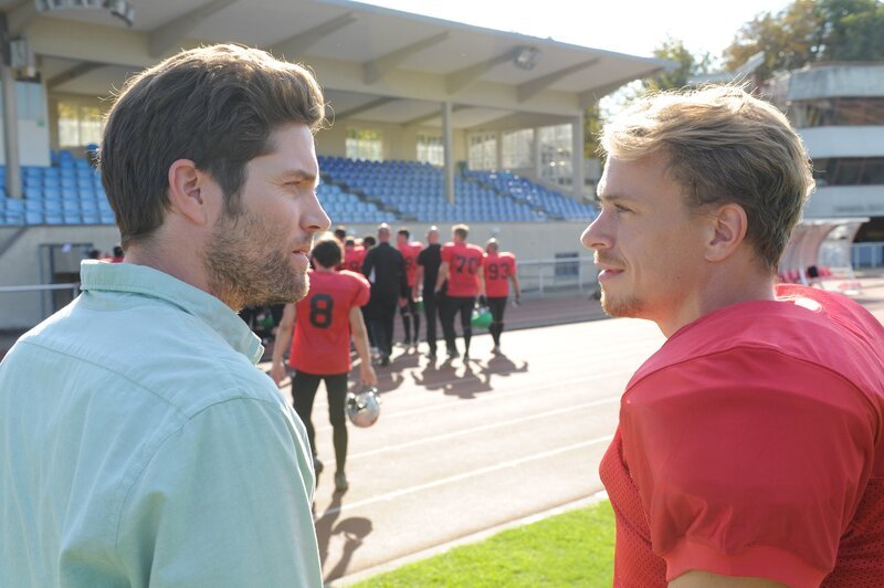 Jo Stoll (Peter Ketnath, l.) befragt Phil Poschner (Matthias Ludwig, r.), der illegale Dopingmittel vertreibt. Die anderen Footballspieler (Komparsen) sind auf dem Weg in die Kabinen. – Bild: ZDF/​MARKUS-FENCHEL