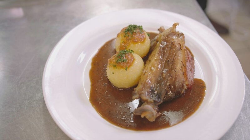 Hauptgericht – Schweinsschäuferl vom bayrischen Strohschwein in Dunkelbiersauce mit Kartoffelknödeln und Speckkrautsalat – des Bräustüberl Schloss Seefeld wird auf einem weißem Teller präsentiert. – Bild: Alica Reisner /​ BR, Bewegte Zeiten Filmproduktion GmbH