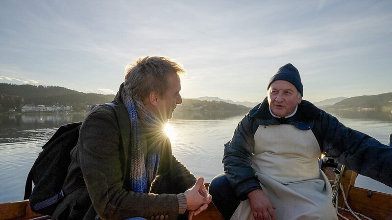 „Der steinerne Fischer“: Hotelwirt und Fischer Seppi Motschiunig berichtet Sagenjäger Max Müller (l.), dass der Fischfang am Wörthersee immer noch auf die gleiche Weise wie zur Zeit der Sage vor über 400 Jahren gehandhabt wird. – Bild: ORF/​Alpha Vision Film