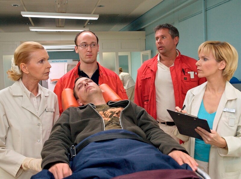 Fabian Althaus (Daniel Krauss, liegend) wird von den Notärzten (Komparsen) in die Sachsenklinik eingeliefert. Dr. Kathrin Globisch (Andrea Kathrin Loewig, re.) und Oberschwester Ingrid (Jutta Kammann, li.) nehmen den Patienten in Empfang. – Bild: MDR/​Krajewsky