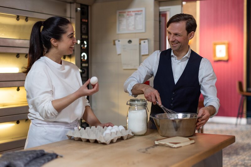 Esma (Özge Delioglan) ist begeistert, als sie tatsächlich mit ihrem Idol Fabian Melzer (Orestes Fiedler) zusammen backen kann. – Bild: RTL /​ Dennis-A.Hundt /​ Flachgelegt