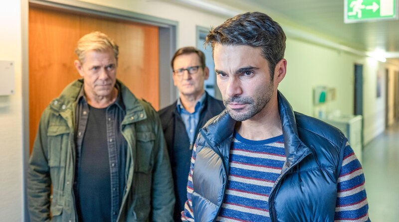 Ivo Struck (Luka Dimić, r.) kann nicht fassen, dass jemand versucht hat, seine Ehefrau Anna umzubringen. Den Kommissaren Finn (Sven Martinek, l.) und Lars (Ingo Naujoks, h.M.) gegenüber äußert er einen Verdacht. – Bild: ORF/​ONE GATE/​ARD/​Thorsten Jander
