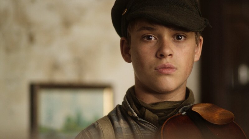 In der von Nazideutschland besetzten Ukraine hat sich der zwölfjährige Waise und Geigenspieler Mitka einer Gruppe von Partisan:innen angeschlossen, die die Unscheinbarkeit des Jungen nutzen, um unbemerkt ein Sprengstoffattentat zu planen. Als sich eine Gruppe hochrangiger SS-Offiziere in ihrer Nähe einfindet, werden diese als Ziel des Attentats auserkoren, wodurch Mitka jedoch auch seinen einzigen Freund in tödliche Gefahr zu bringen droht. – Bild: SWR/​Filmakademie Baden-Württemberg/​Leonard Frederic Caspari