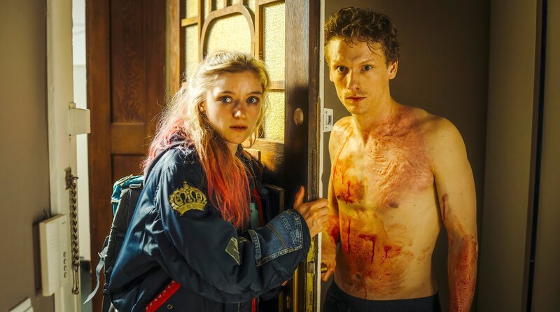 Von links: Kara Roth (Lara Feith) steht Mike Werner (Daniel Noel Fleischmann) an der Wohnungstür gegenüber, der blutverschmiert ist. – Bild: BR/​NEUESUPER GmbH/​Hendrik Heiden/​Bildmanagement