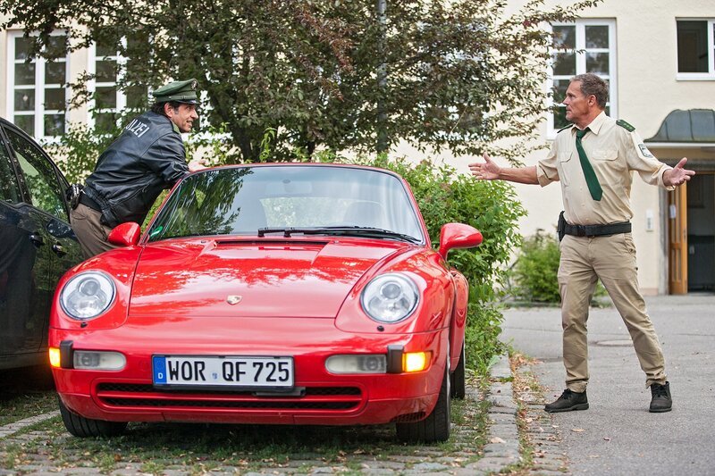 Hubert (Christian Tramitz, rechts) und Staller (Helmfried von Lüttichau, links) machen sich an dem Auto von Dr. Bähr zu schaffen. – Bild: ARD/​TMG/​Christian Hirschhäuser