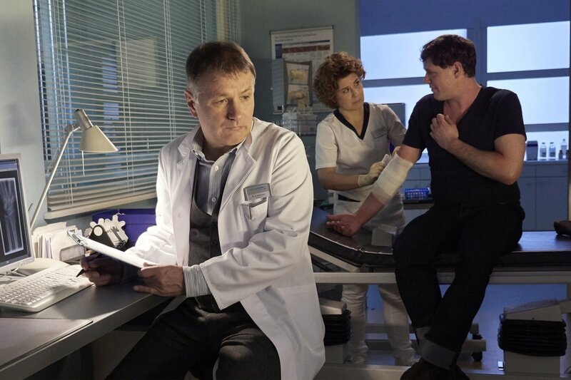 Schwester Ulrike (Anita Vulesica, Mitte) versucht, die blutig gekratzten Stellen an Lorenz Hanfelds (Björn Bugri, rechts) Arm zu verbinden, doch es fällt ihm schwer ruhig zu sitzen. Nach vielen Arztbesuchen, hat noch niemand herausgefunden, was zu dem starken Juckreiz führt. Dr. Roland Heilmann (Thomas Rühmann) möchte weitere Untersuchungen machen, doch Lorenz geht davon aus, dass auch hier, in der Sachsenklinik, keine Ursache gefunden wird. Er hat aufgegeben und geht mittlerweile von einer Zwangsstörung aus. – Bild: MDR/​MDR/​Saxonia Media/​Wernicke