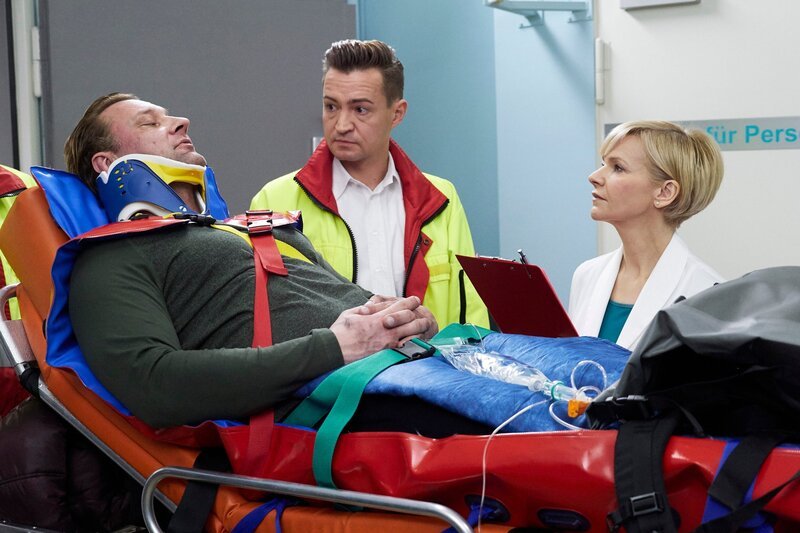 Adrian Walter (Marko Dyrlich, li.) wird nach einem Fahrradunfall vom Notarzt (Markus Neumann, mi.) in die Sachsenklinik eingeliefert. Dr. Kathrin Globisch (Andrea Kathrin Loewig, re.) wundert sich, dass Adrian so wenig Schmerzmittel braucht und auch, dass er in seinem Zustand noch in Flirt-Laune ist. – Bild: MDR/​Saxonia/​Wernicke