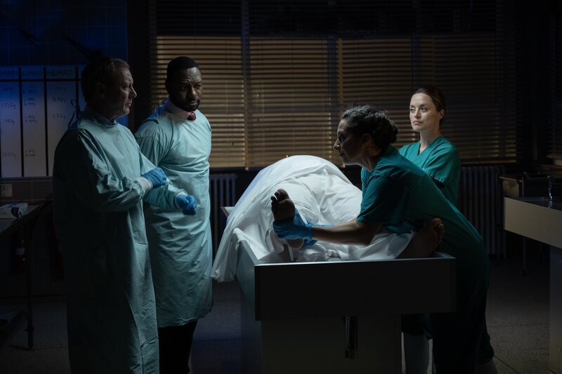 DS Roy Grace (John Simm, l.), DS Glenn Branson (Richie Campbell, 2.v.l.), Cleo (Zoë Tapper, r.) und Nadiuska De Sancha (Carolina Valdé, 2.v.r.) bei der Obduktion der Leiche des stadtbekannten Einbrechers Shelby Stoner (Daniel Fearn): Wie konnte er in Brighton durch den Biss einer exotischen Schlange getötet werden? – Bild: Jonathan Browning /​ ZDF