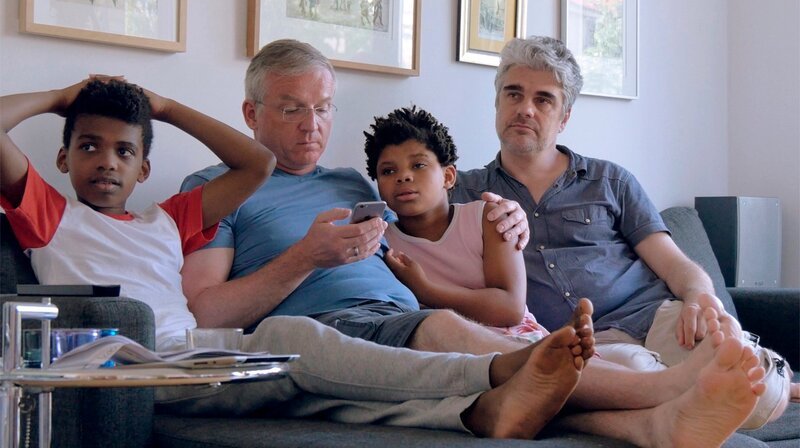 Die beiden Väter Thomas (li) und Ingmar (re.) beim gemeinsamen Fernsehen mit ihren Kindern Julius und Lucy. – Bild: rbb/​Antonia Hungerland