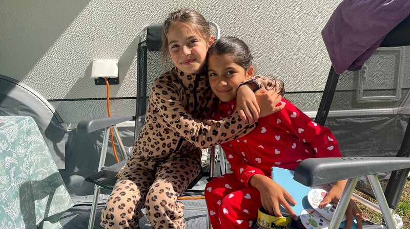 Die Schwestern Serra (9, l) und Ela (8) sitzen am ersten Morgen der Testreise in die Niederlande vor dem Wohnwagen der Karakurts. – Bild: WDR/​Anna Wolter/​Sagamedia