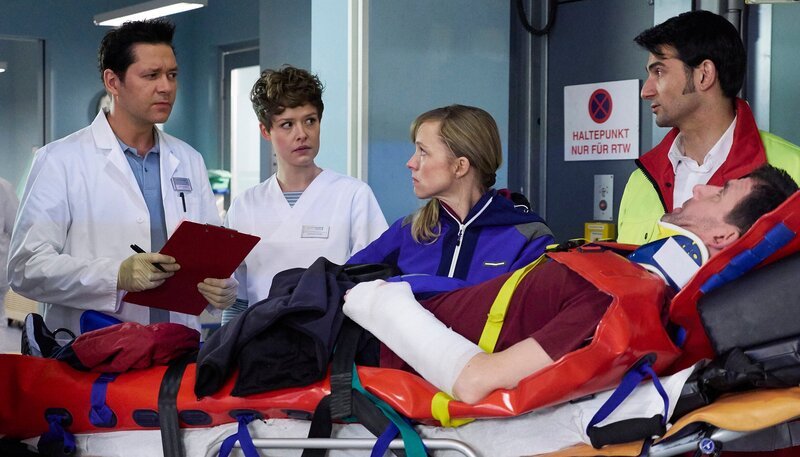 Auf der letzten Testfahrt vor ihrer Weltumrundung per Rad, hatten Nora (Johanna Klante, mi.) und Lutz Kleinschmidt (Thomas Bartling, liegend) einen Unfall. Der Notarzt (Roman Petermann, re.) übergibt die beiden in der Sachsenklinik an Dr. Philipp Brentano (Thomas Koch, li.) und Schwester Svenja Werth (Laura Louisa Garde, 2.v.li.). – Bild: MDR/​Saxonia/​Wernicke