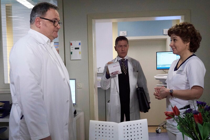 Hans-Peter Brenner (Michael Trischan, li.) soll das erste Mal auf der Visite die Patienten vorstellen. Er ist so aufgeregt, dass er vor Schwester Ulrike (Anita Vulesica) einen Probevortrag hält. Ausgerechnet Dr. Kaminski (Udo Schenk, mi.) platzt in dieser Situation ins Schwesternzimmer und erkundigt sich, ob neben Brenners Entertainmentprogramm Zeit für einen wichtigen Gang ins Labor bleibt. – Bild: MDR/​Saxonia Media Filmproduktion/​Wernicke