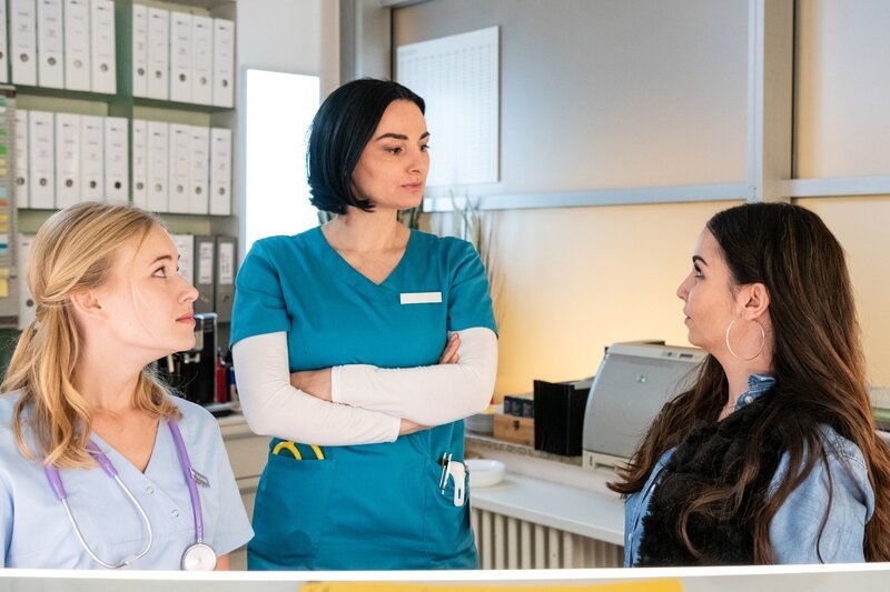 Um das Team zu entlasten, hilft Samira (Sila Sahin-Radlinger, r.) am Empfang der Station aus. Kiki (Valerie Huber, l.) und Nora (Mimi Fiedler, M.) sehen das mit gemischten Gefühlen. – Bild: TVNOW