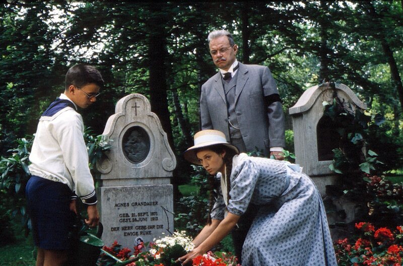 Karl Grandauer (Jörg Hube) besucht mit seinen Kindern Luise Grandauer (Sandra White) und Karli Grandauer (N.N.) das Grab seiner verstorbenen Frau. – Bild: BR/​Tellux-Film GmbH