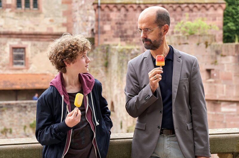 Ingolf (Christoph Maria Herbst) möchte mit seinem Adoptivsohn Ole (Nico Ramon Kleemann) mehr Zeit verbringen und schlendern durch Heidelberg und essen zusammen Eis. – Bild: PLURIMEDIA (ARD Degeto /​ Frank Dicks)