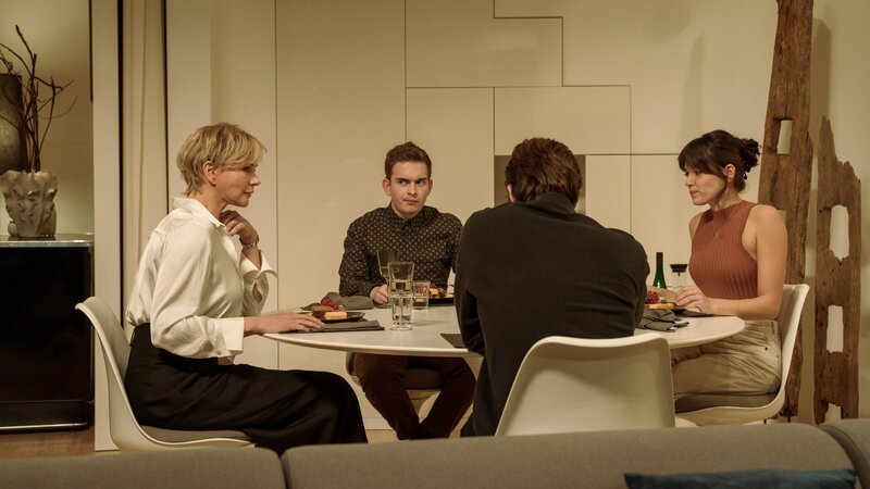 Ein gemütliches Abendessen in unruhigen Zeiten? Regina Mannheimer (Veronica Ferres, l.) hat Finja (Caroline Hartig, r.) eingeladen, um sie besser kennen zu lernen. Ihr ist nicht entgangen, dass Sam (Jonathan Elias Weiske, 2.v.r.) an Finja interessiert ist. Während Sam die Anspielungen seiner Mutter unangenehm sind, amüsiert sich Finja darüber. Jannik (Constantin Keller, 2.v.l.) hingegen ist besorgt. Er hat beobachtet, dass seine Mutter etwas im Garten verbrannt hat. Macht Regina nur gute Miene zu bösem Spiel? – Bild: Roland Guido Marx /​ ZDF