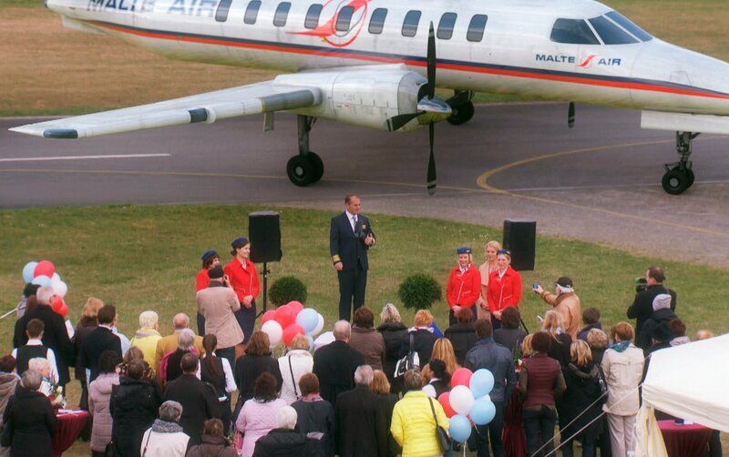 Festliche Stimmung auf dem Flugplatz Uelzen: Malte Neumann (Marcus Bluhm, M.) begrüßt die geladenen Gäste und gibt den Start seiner Fluglinie „Malte-Air“ bekannt. – Bild: ARD/​Nicole Manthey