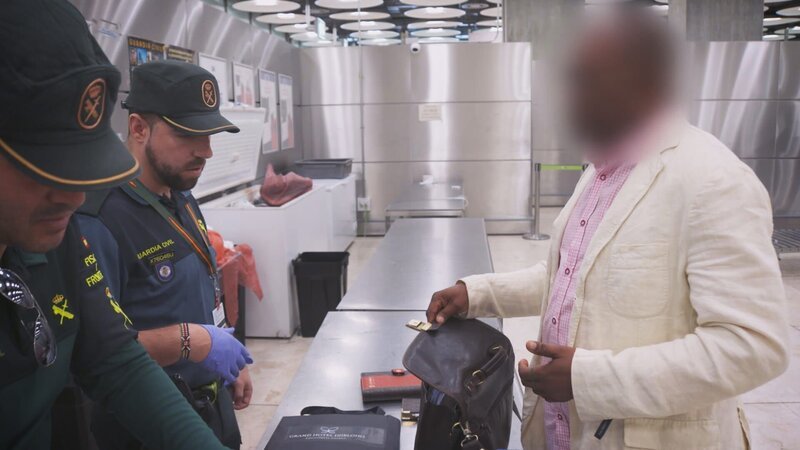 Ein Zollbeamter am Madrider Flughafen kontrolliert das Gepäck eines Passagiers – Bild: Warner Bros. Discovery