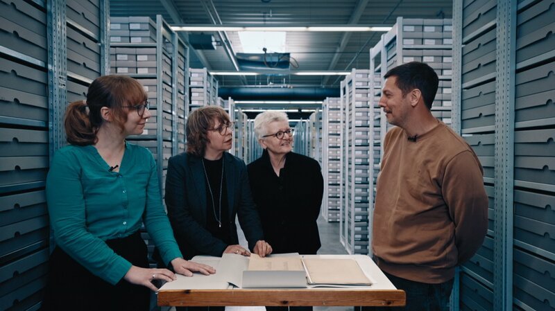 Von links: Franziska Schubert, Anke Münster, Dorothee Schmitz-Köster und Thilo Mischke. Sie stehen gemeinsam in den Arolsen Archives und schauen auf Akten zu Thilo Mischkes Urgroßvater. – Bild: ZDF und Leonard Schmidt