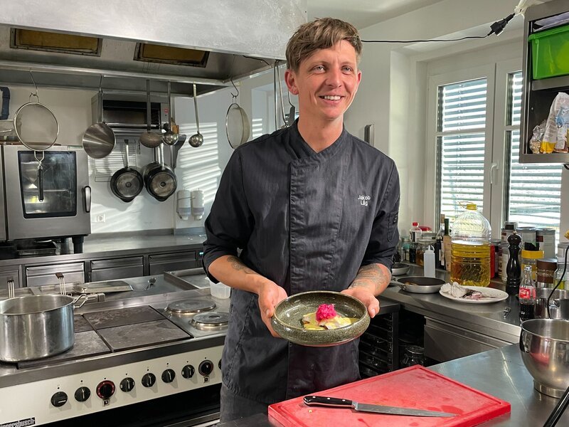 Koch und Patron Jakob Lilg in der Küche des Restaurants Löwenzahn mit eingelegter Rotfeder. – Bild: ORF/​Satel Film/​David Haslinger