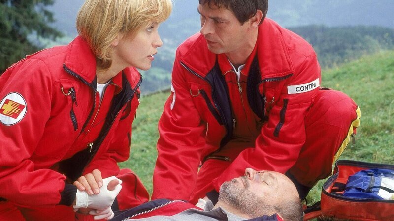 Hans Zimmer (Peter Mazzuchelli) wurde von einer kleinen Privatmaschine im Tiefflug so lange gejagt, bis er einen Abhang hinuntergestürzt ist. Verletzt wartete er auf die Rettungsärzte. Contini (Tom Mikulla) und Dr. Thaler (Roswitha Meyer) versorgen ihn für den Flug in die Klinik. – Bild: RTL /​ Miguel Dieterich
