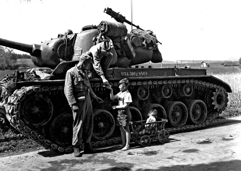 Österreich 25.05.1951 – Übung „Rebound“: Sgt. Donald A.Ziesmer (Kalispell, Montana) und Sgt. William P.Kratzenberg (Pittsburg, Pa), Mitglieder der Medium Tank Company, verschenken Süssigkeiten an zwei österrreichische Kinder, die ihren Panzer bewundern. – Bild: ORF III