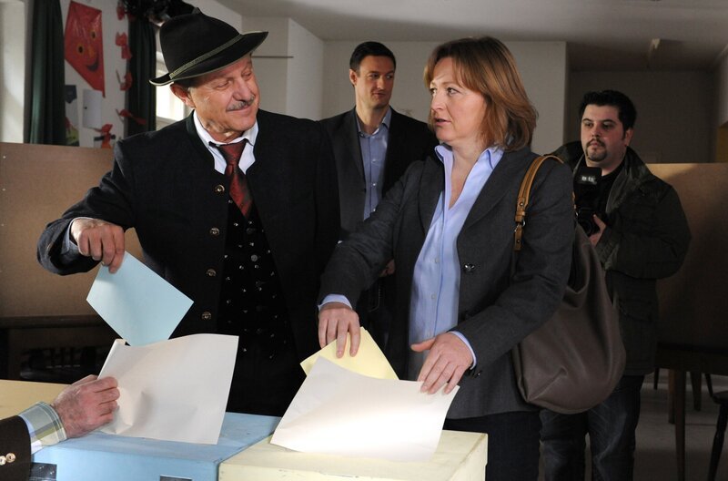 Bürgermeisterkandidatin Vroni nimmt die Spöttelei des Amtsinhabers gelassen hin. Von links: Lorenz Schattenhofer (Werner Rom), KLD und Veronika Brunner (Senta Auth). – Bild: BR/​Marco Orlando Pichler
